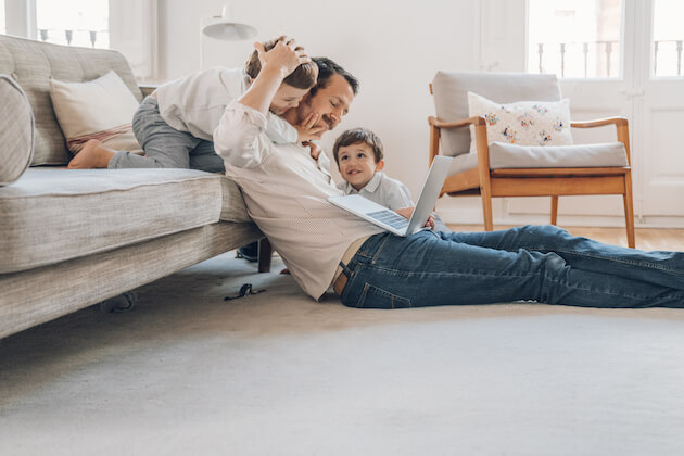 father sitting on floor next to couch with two children