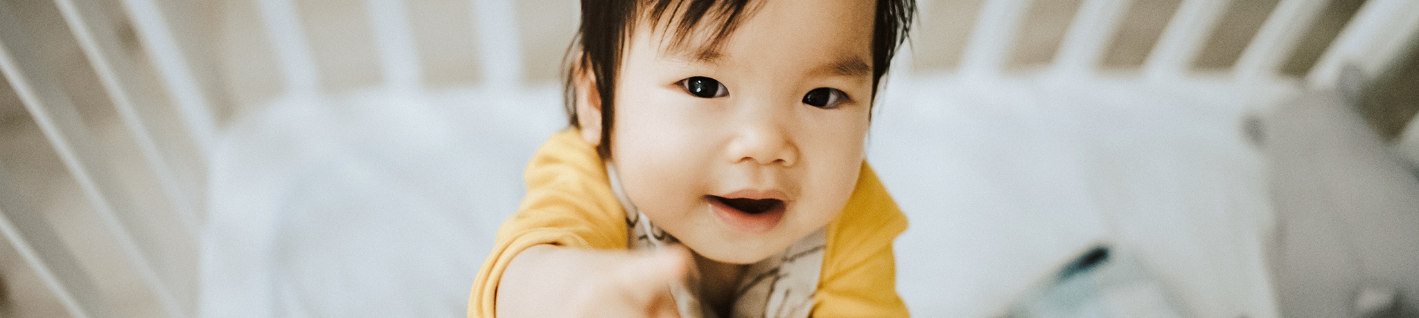 Baby in crib pointing at camera