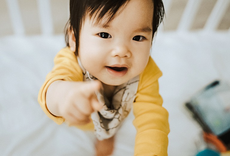 Baby in crib pointing at camera