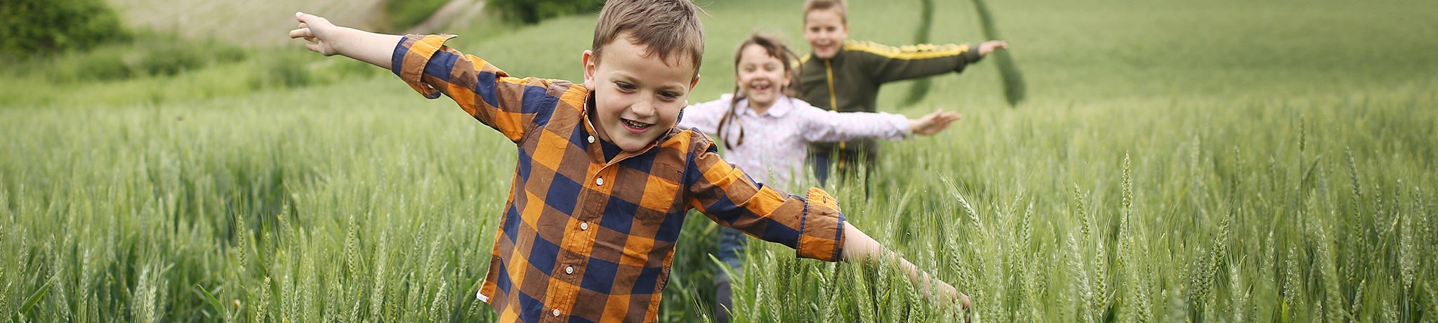 Three children running in grass field with arms stretched out