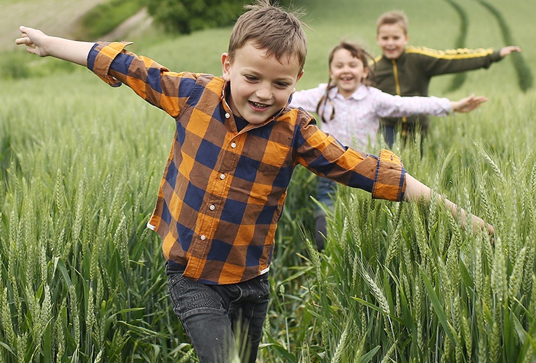 Three children running in grass field with arms stretched out