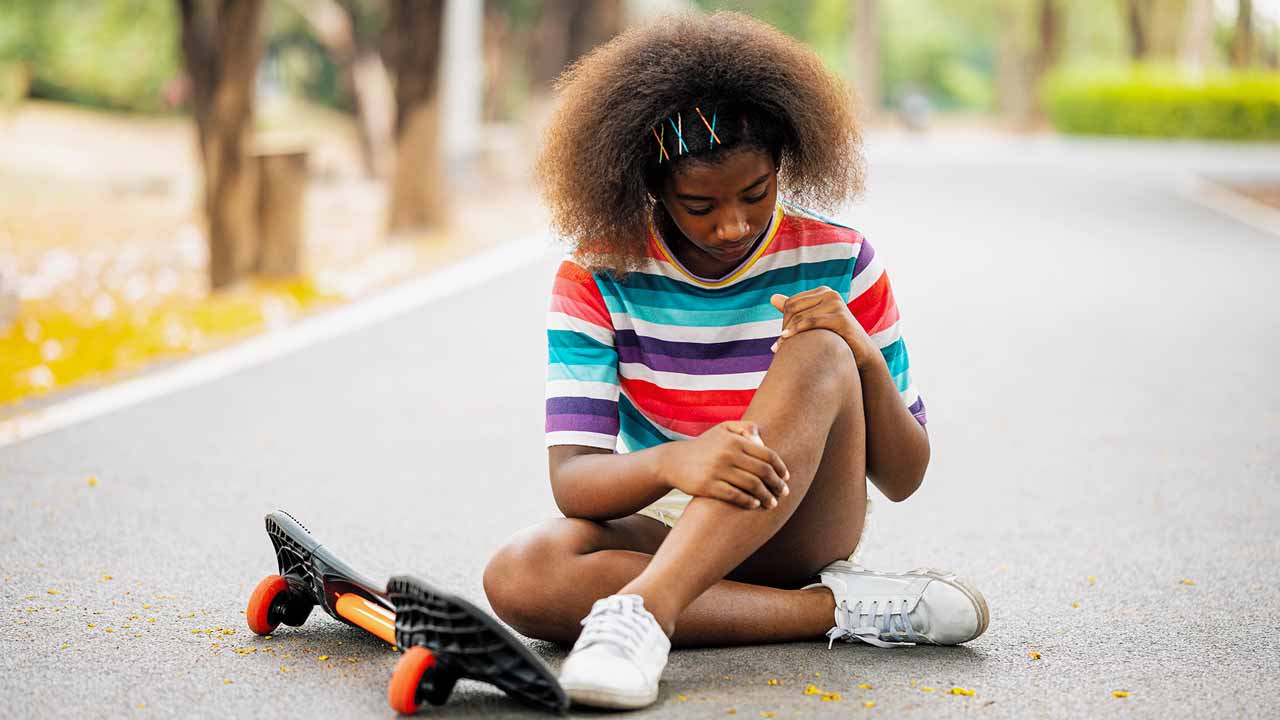 Young girl assessing her knee sprain after falling off of skateboard