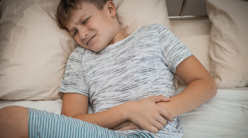 Boy holding stomach in pain on bed