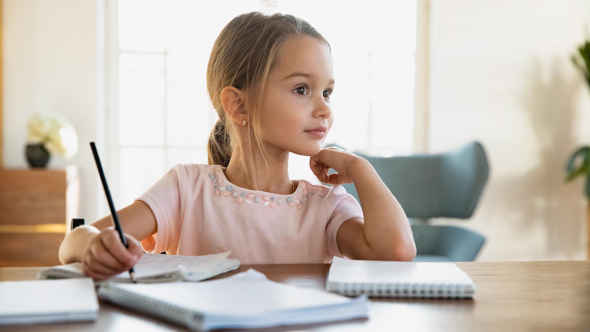 Smiling little girl dreaming distracted from studying at home