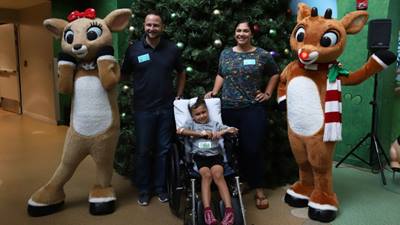 A young boy and his family pose happily by the Christmas tree at Arnold Palmer Hospital.